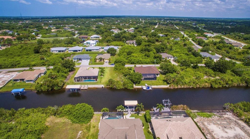An aerial view shows houses along a canal with boat docks and surrounding green vegetation — 9386 BLUEGILL CIRCLE, PORT CHARLOTTE, FL