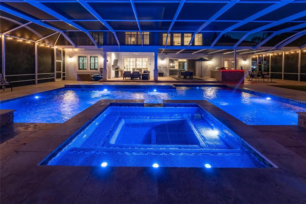 A backyard swimming pool and hot tub are illuminated at night under a screened enclosure — 613 BALIBAY ROAD, APOLLO BEACH, FL