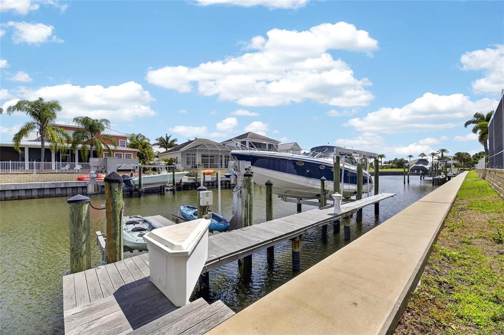 A canal view featuring a wooden dock, a boat lift with a boat, and houses — 613 BALIBAY ROAD, APOLLO BEACH, FL