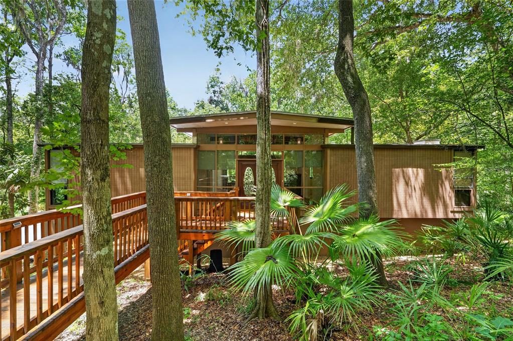 A wooden house with a deck and large windows is nestled among trees in a forest — 2032 NW 24TH STREET, GAINESVILLE, FL