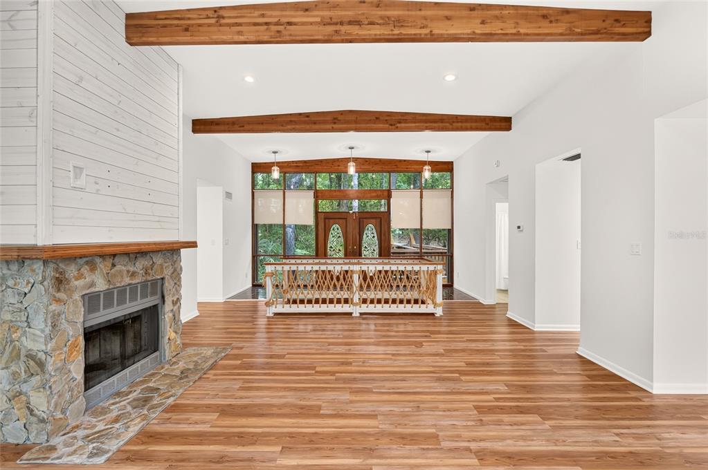 A living room features a stone fireplace, wood-look flooring, exposed ceiling beams, and a wooden entryway — 2032 NW 24TH STREET, GAINESVILLE, FL