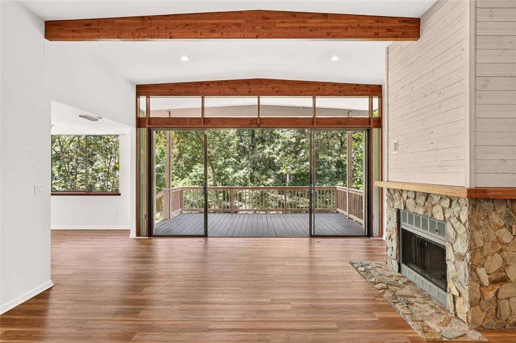 A living room with wood flooring, a stone fireplace, and sliding doors opening to a deck — 2032 NW 24TH STREET, GAINESVILLE, FL