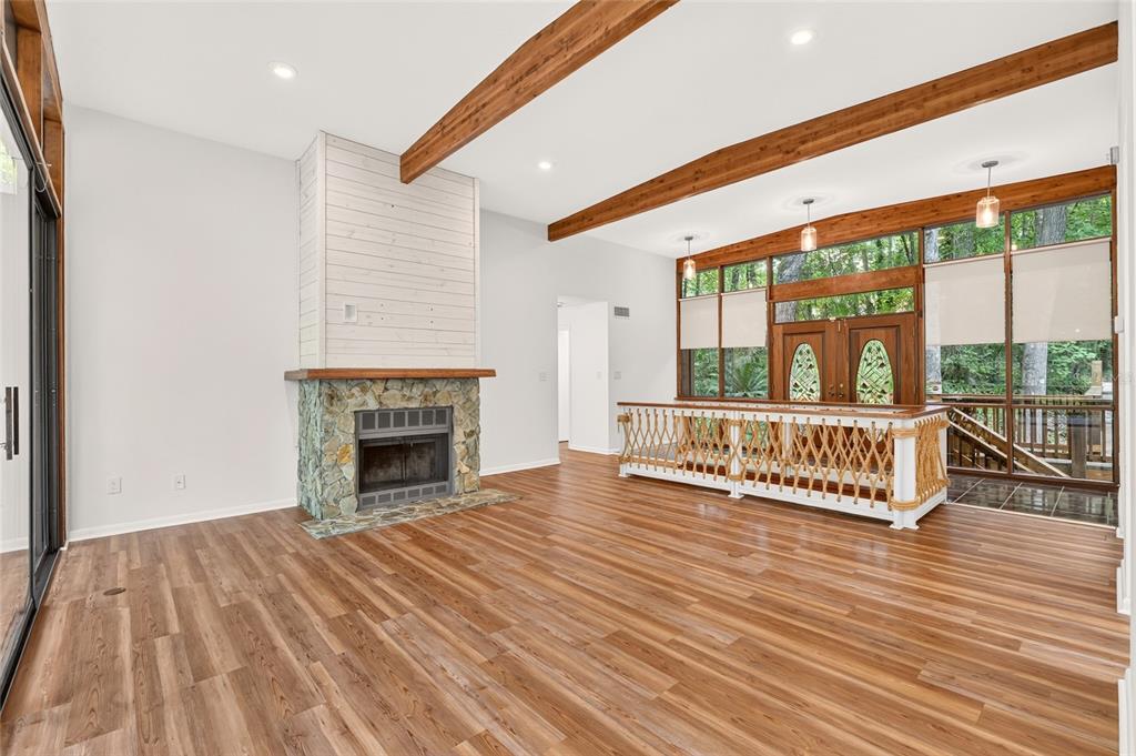 A living room features wood-look flooring, a stone fireplace, exposed ceiling beams, and large windows — 2032 NW 24TH STREET, GAINESVILLE, FL