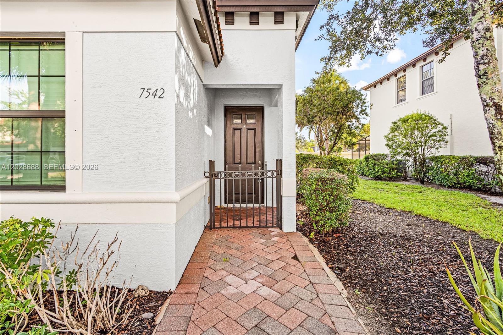 A brick walkway leads to a gated entryway with a dark brown door — 7542 Bristol Cir, Naples FL 34120, NAPLES, FL