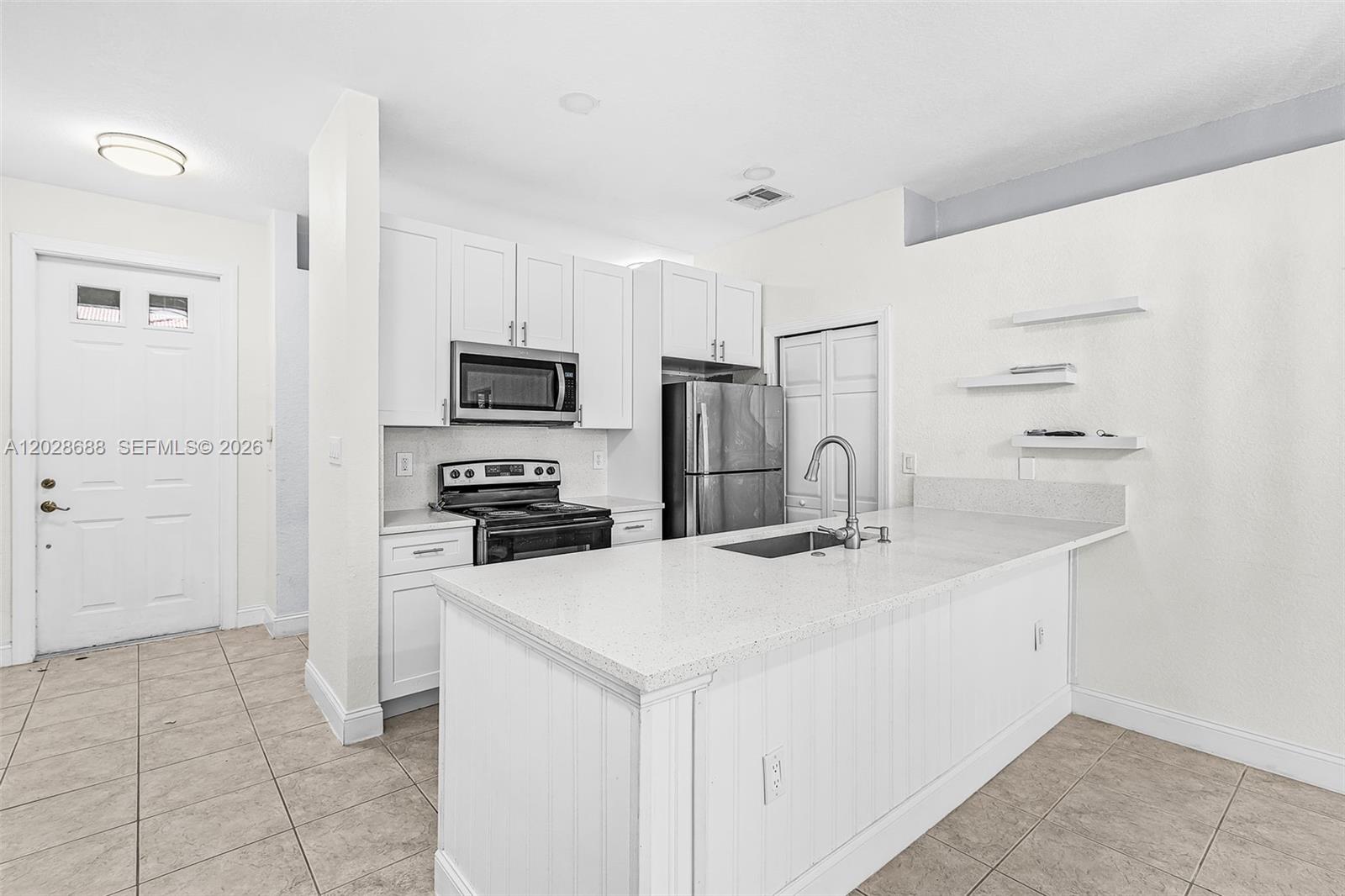 A kitchen features white cabinets, stainless steel appliances, and a quartz-topped island with a sink — 7542 Bristol Cir, Naples FL 34120, NAPLES, FL