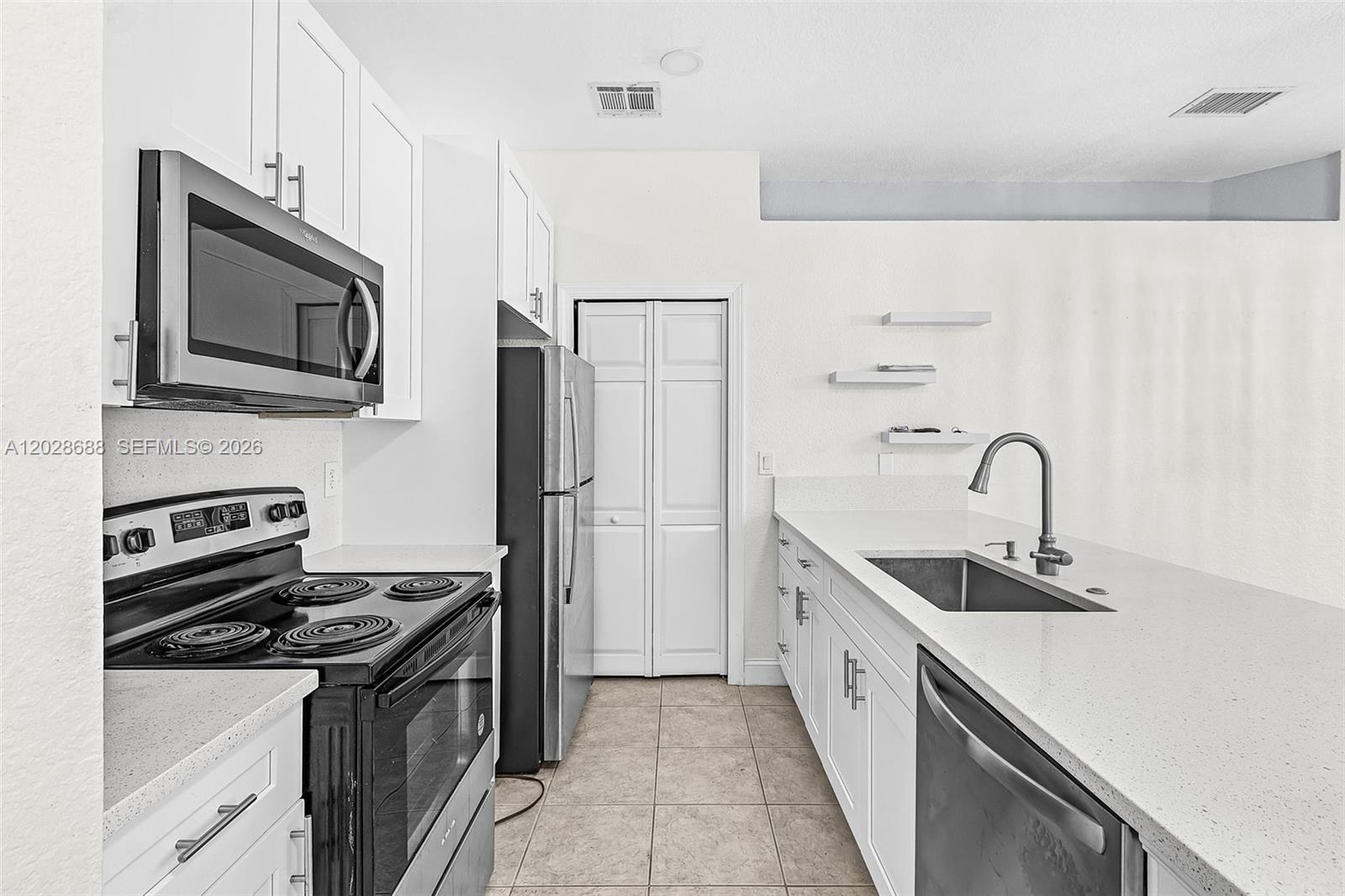 A kitchen features white cabinetry, black appliances, a stainless steel sink, and light-colored countertops — 7542 Bristol Cir, Naples FL 34120, NAPLES, FL