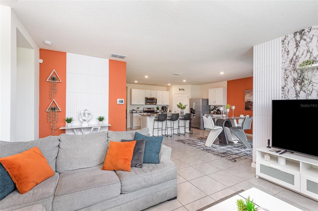 A living room with a grey sofa and orange accents opens into a kitchen and dining area — 1031 AUGUST SKY DRIVE, DELTONA, FL
