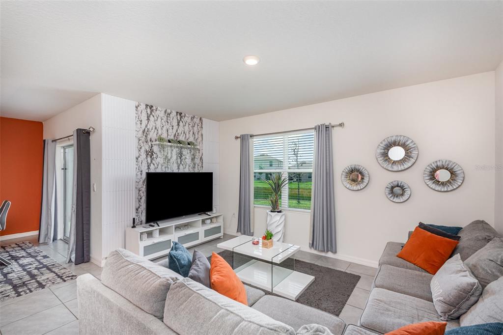 A living room features a marble-accented media wall, gray sectional sofa, and a glass coffee table — 1031 AUGUST SKY DRIVE, DELTONA, FL
