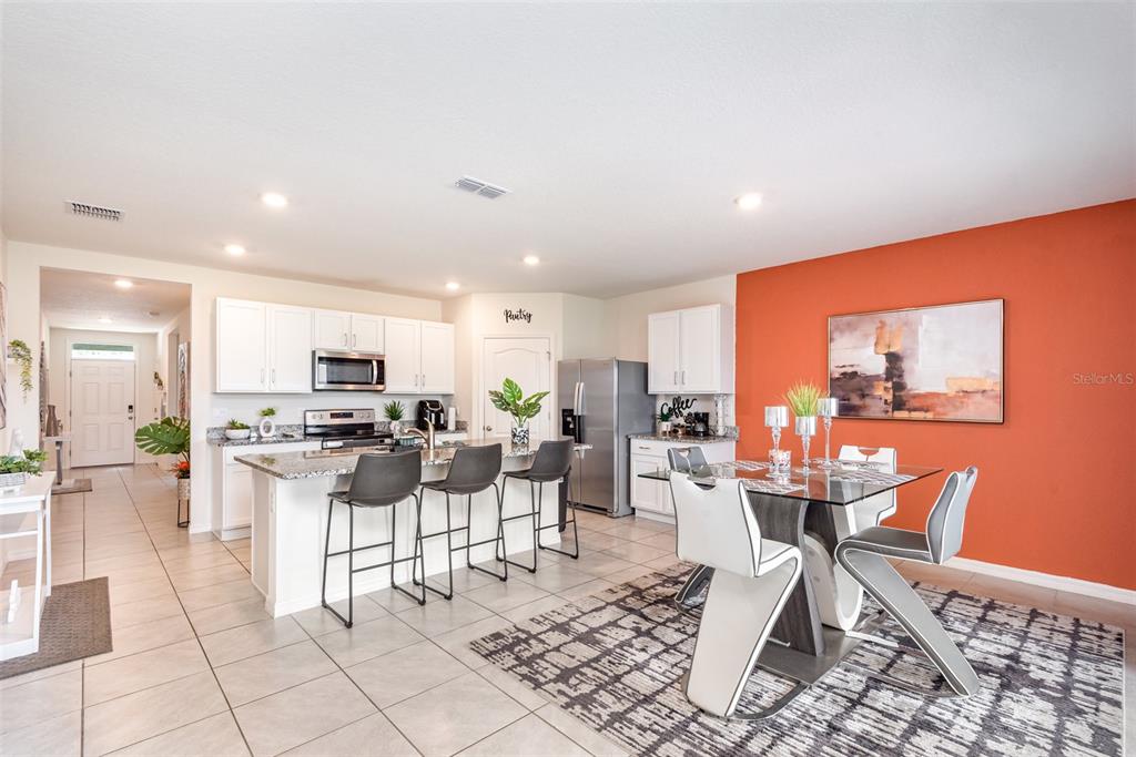An open-concept kitchen and dining area features white cabinetry, granite countertops, and an orange wall — 1031 AUGUST SKY DRIVE, DELTONA, FL