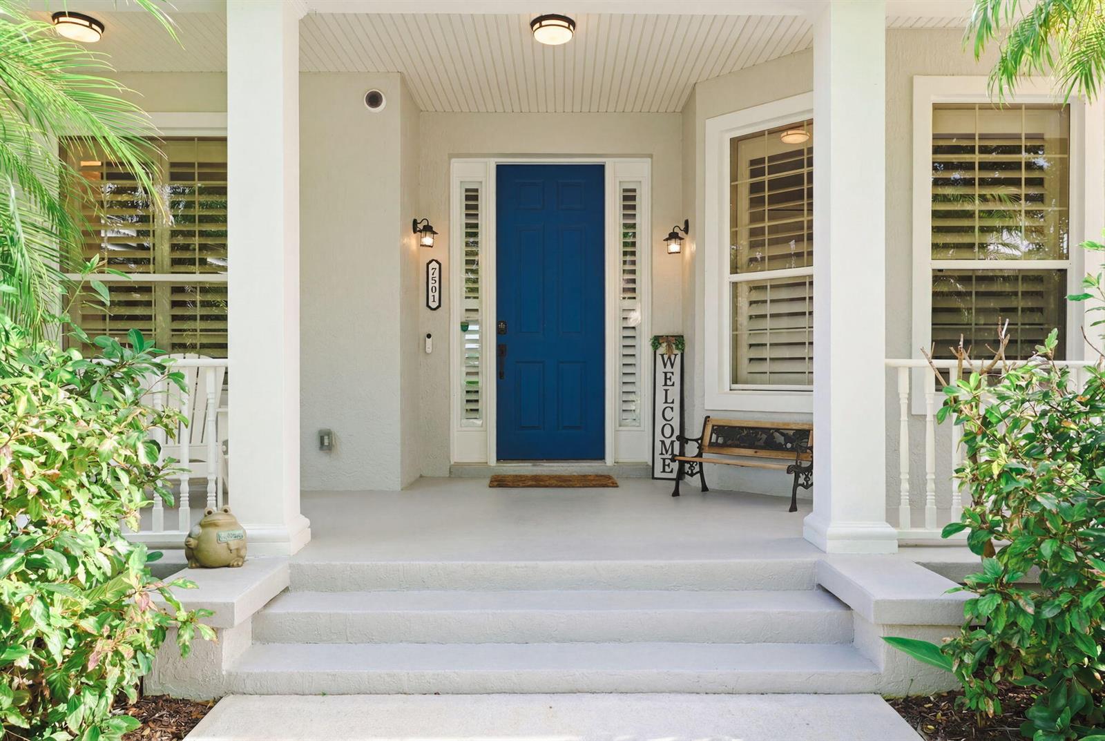 A front porch with a blue door, white columns, and a small wooden bench — 7501 14th Lane, Vero Beach FL 32966, VERO BEACH, FL