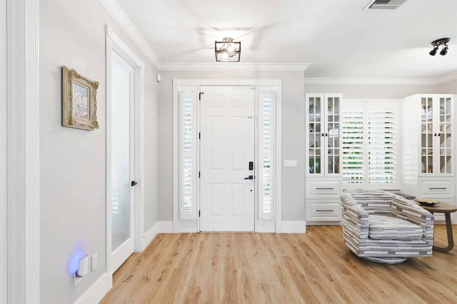 A bright entryway features light wood flooring, a white front door, and built-in display cabinets — 7501 14th Lane, Vero Beach FL 32966, VERO BEACH, FL
