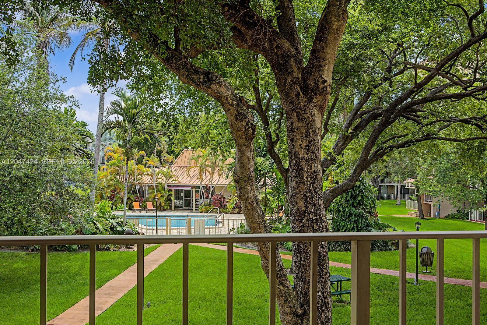 A view from a balcony overlooking a swimming pool, lawn, and mature trees — 13120 SW 92nd Ave # 207, Miami FL 33176, MIAMI, FL