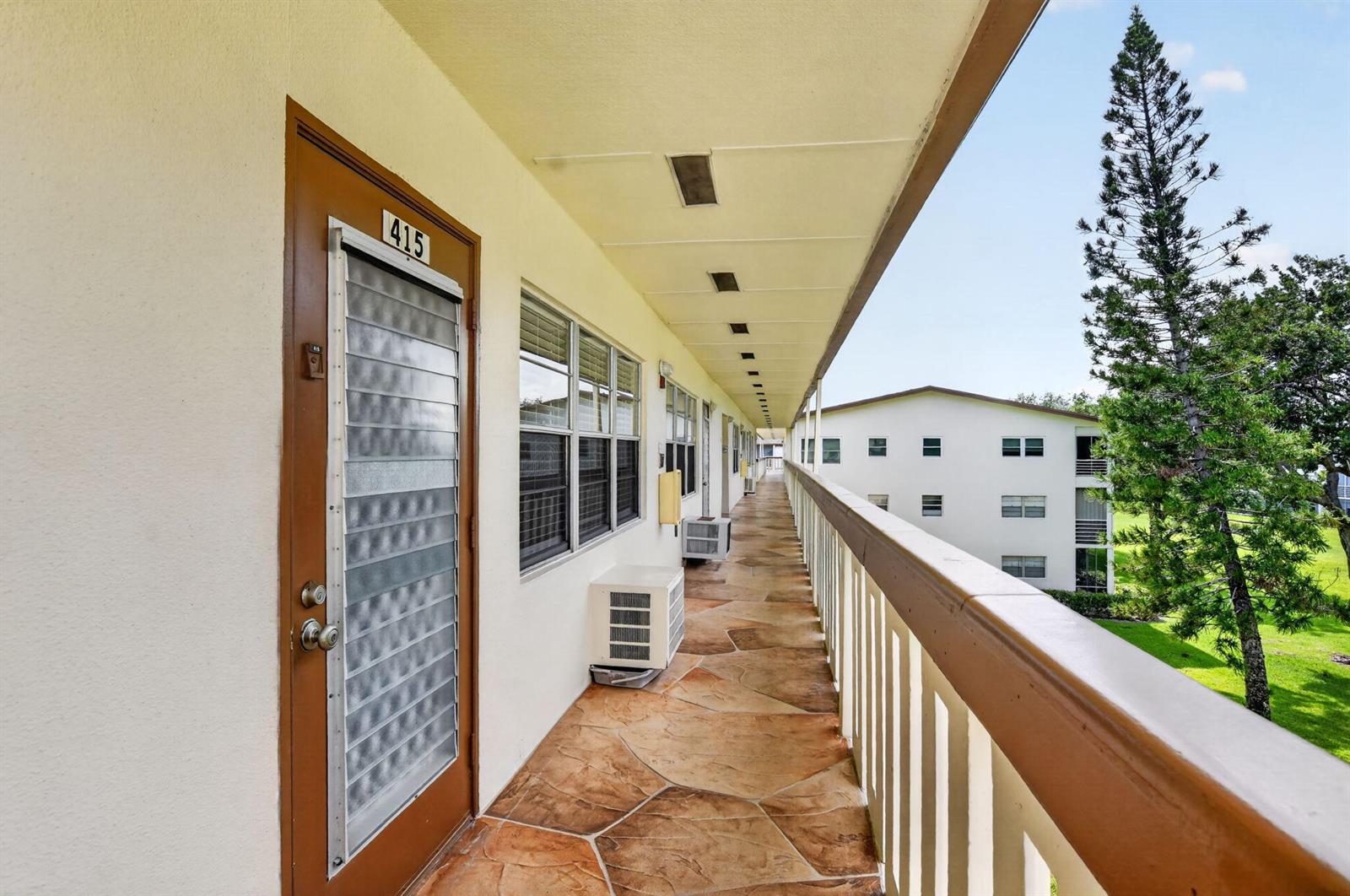 An outdoor apartment walkway features stone-patterned flooring, a brown door numbered 415, and railings — 415 Mansfield # J, Boca Raton FL 33434, BOCA RATON, FL