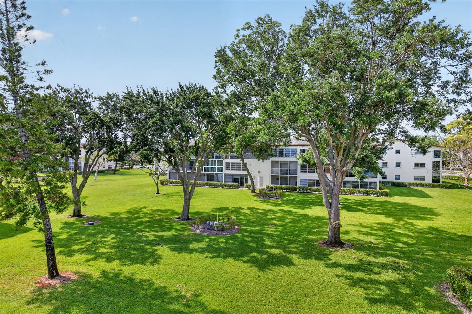 A multi-story apartment building sits behind a large, grassy lawn with several mature trees — 415 Mansfield # J, Boca Raton FL 33434, BOCA RATON, FL