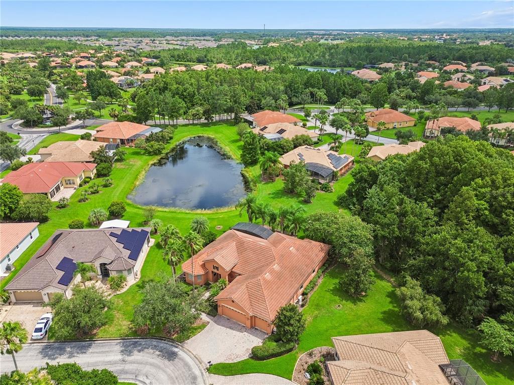 An aerial view shows a suburban neighborhood with houses, a central pond, and lush landscaping — 501 MONTAGE LN, POINCIANA, FL