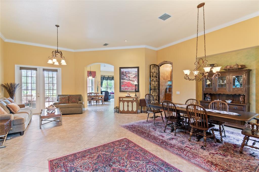 A spacious living and dining area with tile floors, yellow walls, and two ornate chandeliers — 501 MONTAGE LN, POINCIANA, FL