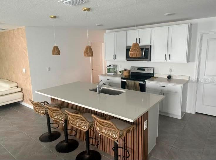 A kitchen features white cabinets, a large island with a sink, and three rattan barstools — 37389 SHARKS EYE LANE, ZEPHYRHILLS, FL
