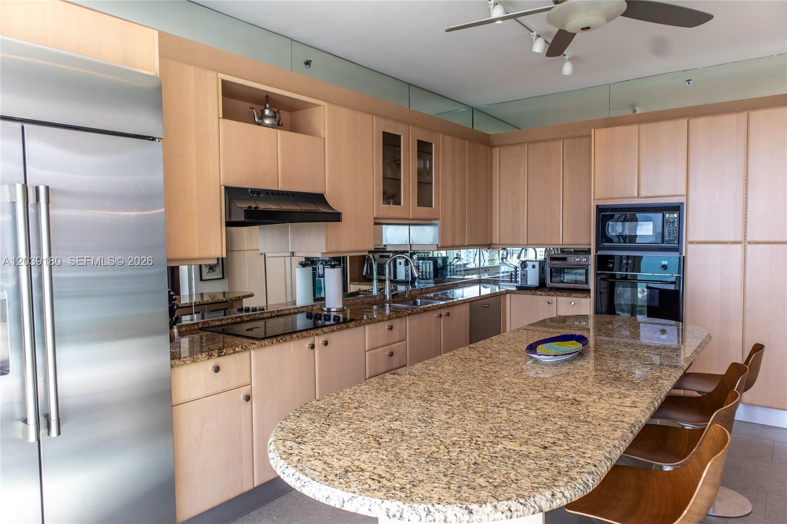A kitchen with light wood cabinets, granite countertops, stainless steel appliances, and a curved island — 300 S Pointe Dr # 1502, Miami Beach FL 33139, MIAMI BEACH, FL