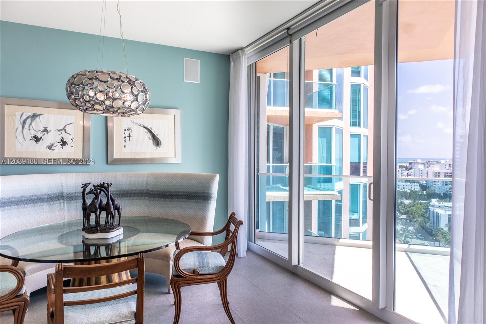 A dining area features a glass table, curved banquette, and floor-to-ceiling windows overlooking the ocean — 300 S Pointe Dr # 1502, Miami Beach FL 33139, MIAMI BEACH, FL
