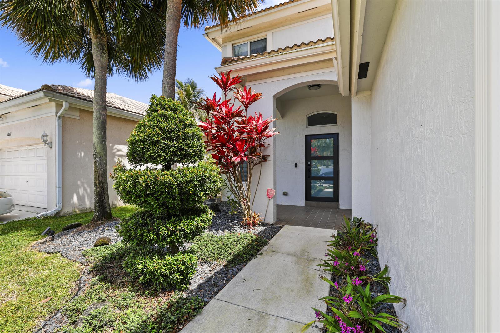 The exterior of a white house features a front walkway, a red plant, and landscaping — 6878 NW 33rd Street, Margate FL 33063, MARGATE, FL
