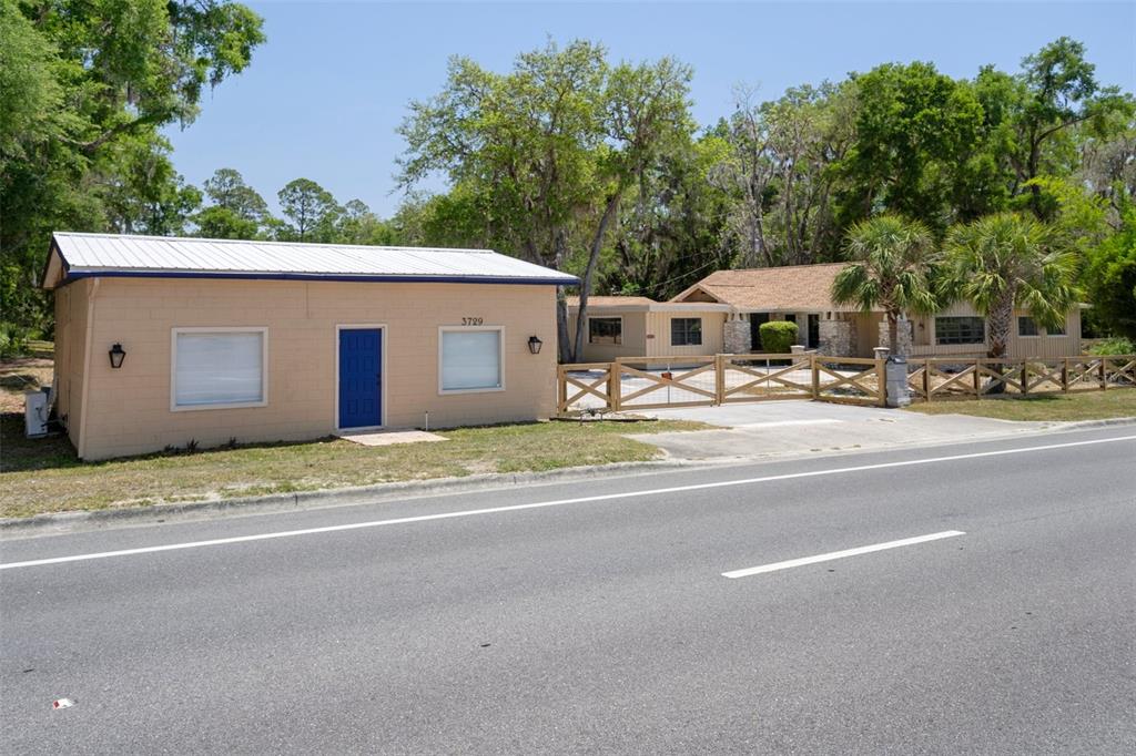 A tan, single-story building with a blue door sits beside a house behind a fence — 3729 S LECANTO HIGHWAY, LECANTO, FL