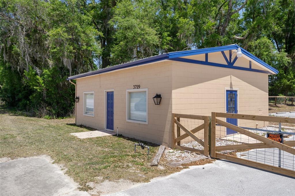 A beige concrete block building with blue trim and doors sits behind a wooden fence — 3729 S LECANTO HIGHWAY, LECANTO, FL