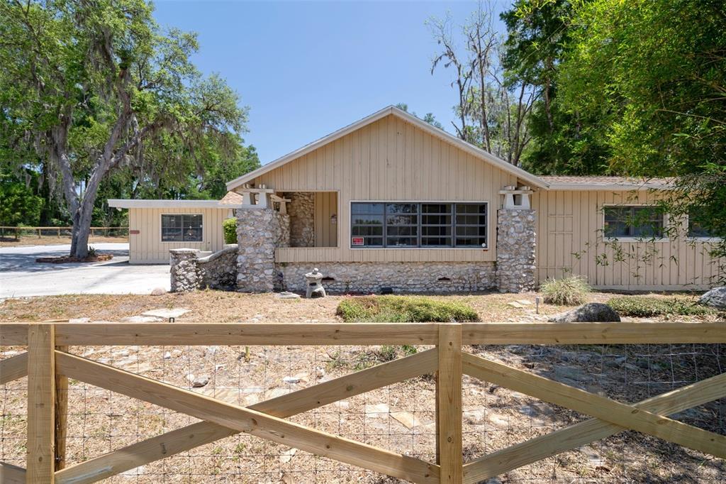 A single-story house with vertical siding and stone accents sits behind a wooden farm fence — 3729 S LECANTO HIGHWAY, LECANTO, FL