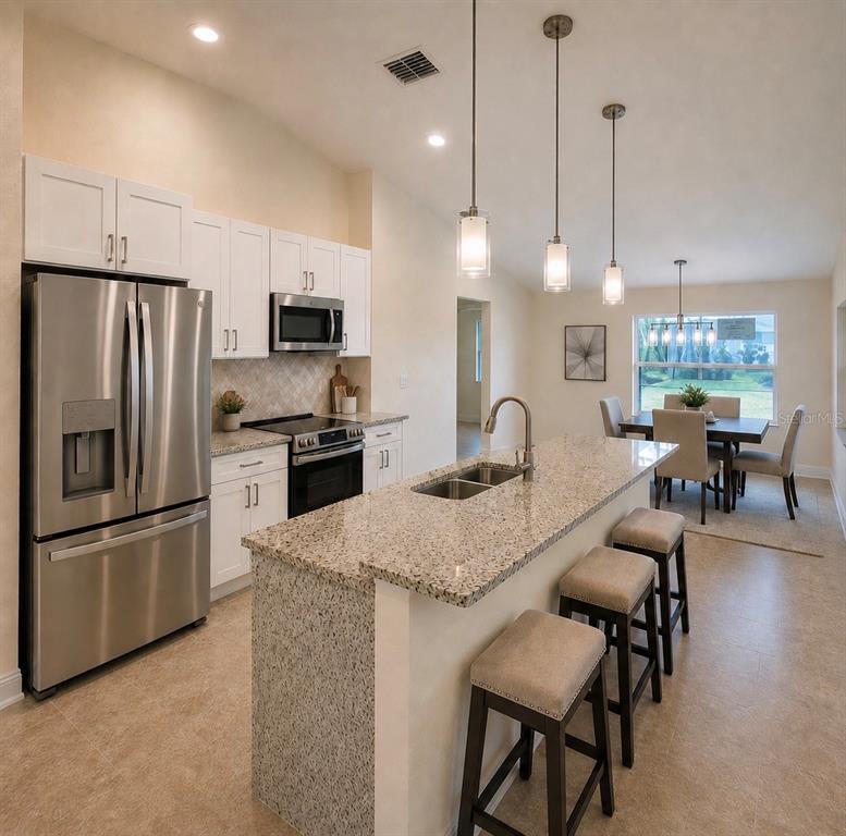A kitchen features white cabinets, granite countertops, a stainless steel refrigerator, and a breakfast bar — 121 MARINER LANE, ROTONDA WEST, FL