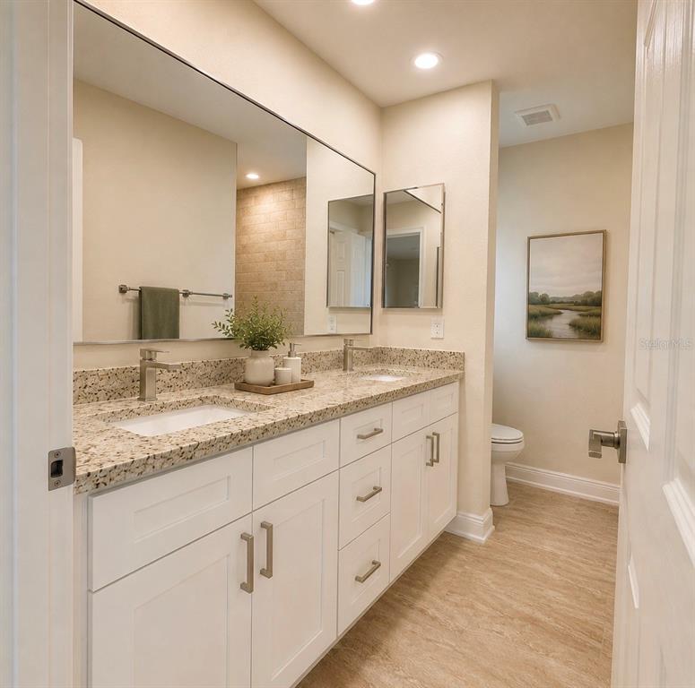 A bathroom features a double vanity with white cabinets, granite countertops, and a large mirror — 121 MARINER LANE, ROTONDA WEST, FL