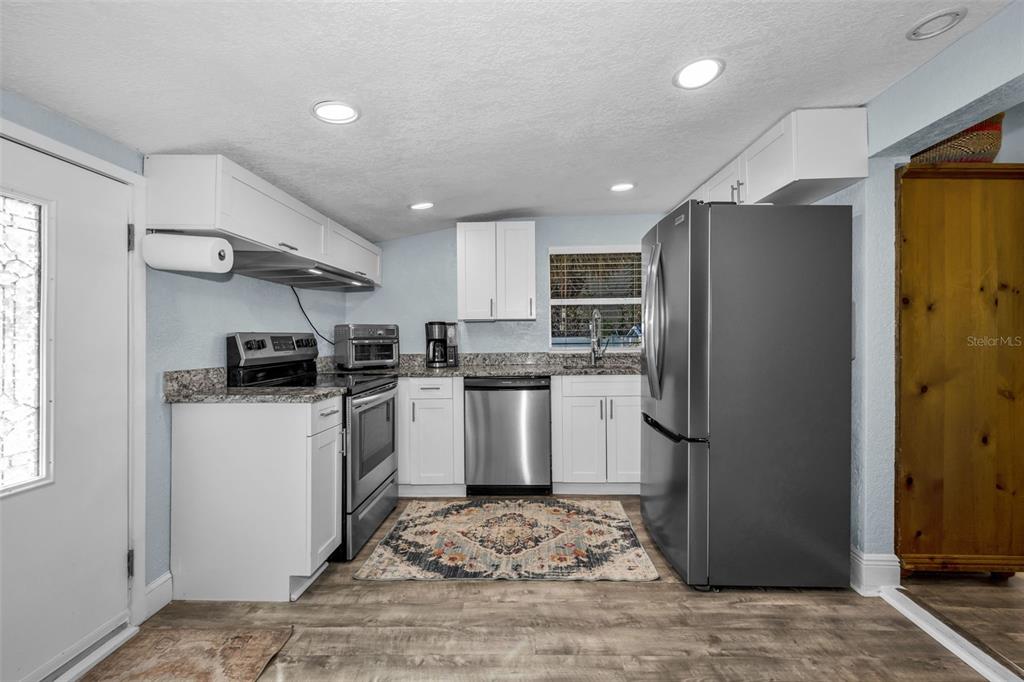 A kitchen features white cabinets, granite countertops, stainless steel appliances, and wood-look flooring — 504 70TH AVENUE, ST PETE BEACH, FL