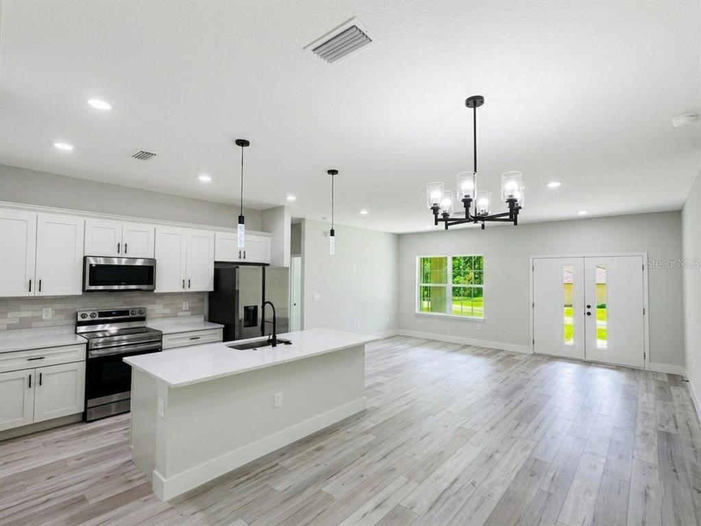 A modern kitchen features white cabinets, a central island, and light wood-look flooring — 8106 N GALENA AVENUE, CITRUS SPRINGS, FL