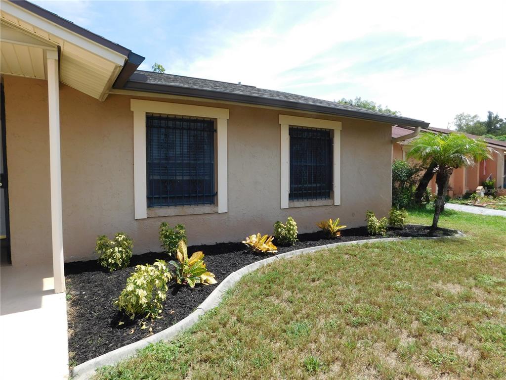A tan stucco house exterior features two windows with security bars and a landscaped garden — 2311 TOWERBRIDGE STREET, ORLANDO, FL