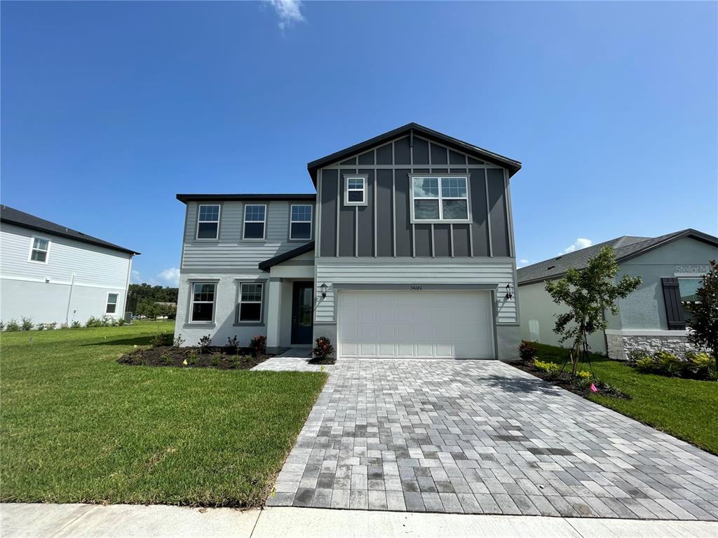 A two-story house with a gray exterior, board-and-batten siding, and a paved driveway — 34286 EVERGREEN HILL COURT, WESLEY CHAPEL, FL