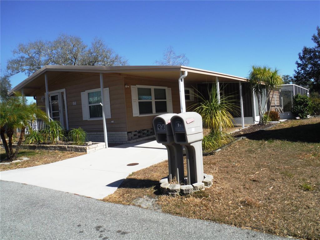 A single-story manufactured home with a tan exterior, a concrete driveway, and two mailboxes — 98 SUGAR BEAR DRIVE UNIT 57, SAFETY HARBOR, FL