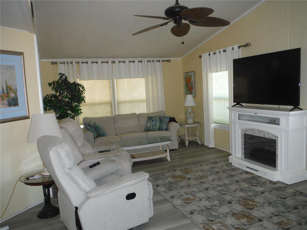 A living room features a fireplace, a ceiling fan, light-colored furniture, and wood-look flooring — 98 SUGAR BEAR DRIVE UNIT 57, SAFETY HARBOR, FL