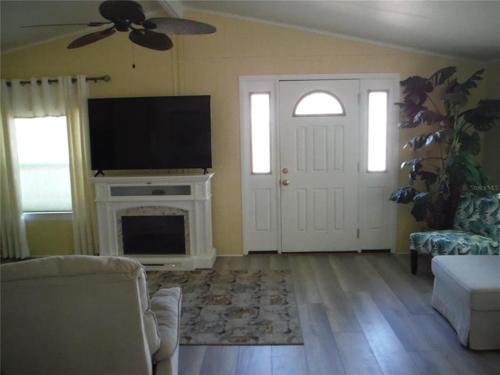 A living room features a fireplace, a wall-mounted television, a front door, and wood-look flooring — 98 SUGAR BEAR DRIVE UNIT 57, SAFETY HARBOR, FL