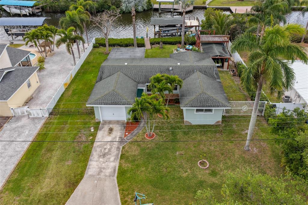 An aerial view shows a single-story house with a green roof, driveway, and backyard canal — 6907 9TH AVENUE NW, BRADENTON, FL