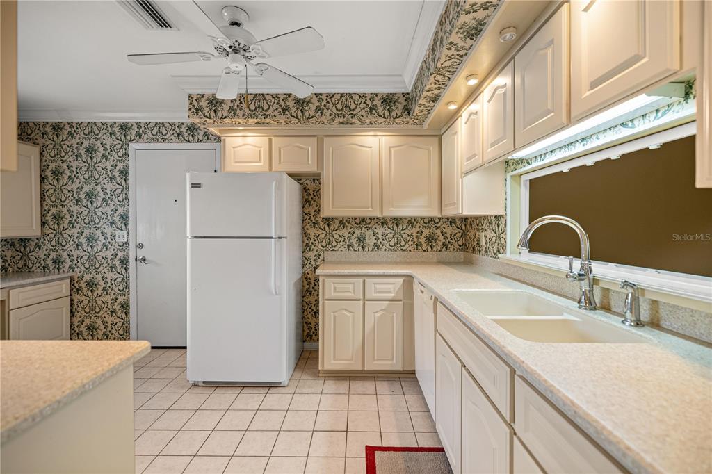 A kitchen features white cabinets, patterned wallpaper, a white refrigerator, and a double-basin sink — 2050 SE 37TH COURT CIRCLE, OCALA, FL