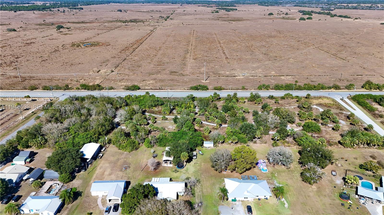 An aerial view shows several houses with yards situated near a road and open fields — 8636 W Hwy 70, Okeechobee FL 34974, OKEECHOBEE, FL