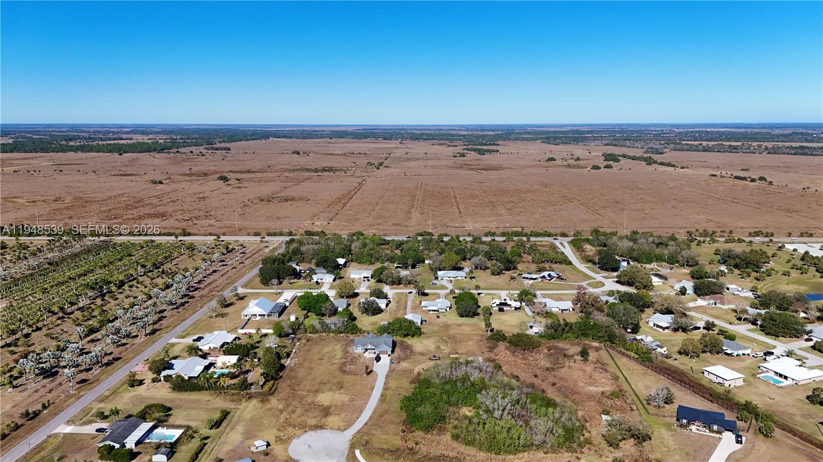 An aerial view shows a residential neighborhood bordering a large, open field — 8636 W Hwy 70, Okeechobee FL 34974, OKEECHOBEE, FL