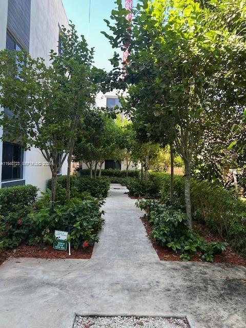 A concrete walkway leads between rows of trees and shrubs toward a modern building exterior — 751 NW 1st St # 305, Miami FL 33128, MIAMI, FL