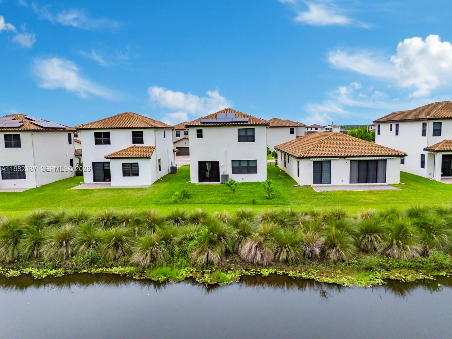 An aerial view shows the rear exteriors of several white houses with tiled roofs near water — 5626 Agostino Way, Ave Maria FL 34142, AVE MARIA, FL