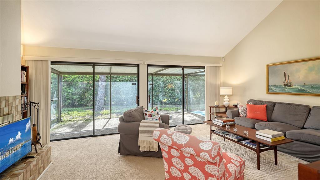 A living room features a vaulted ceiling, sliding glass doors, carpeted floors, and a fireplace — 4983 GREENCROFT ROAD UNIT 181, SARASOTA, FL