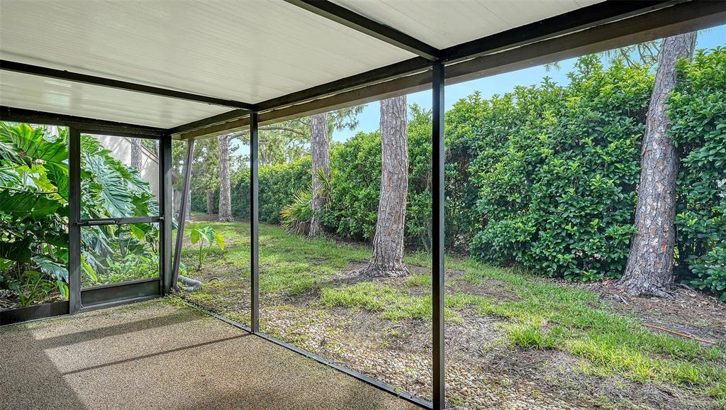 A screened-in patio overlooks a grassy backyard with several tall pine trees and hedges — 4983 GREENCROFT ROAD UNIT 181, SARASOTA, FL
