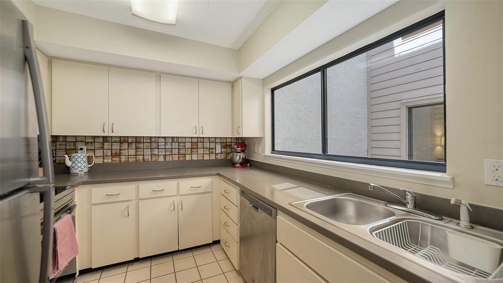 A kitchen features off-white cabinets, a gray countertop, a double sink, and a tiled backsplash — 4983 GREENCROFT ROAD UNIT 181, SARASOTA, FL