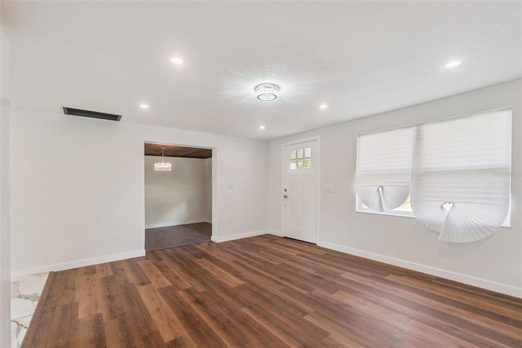 A bright living room features white walls, wood-look flooring, a front door, and recessed lighting — 126 KENSINGTON ROAD, DELAND, FL