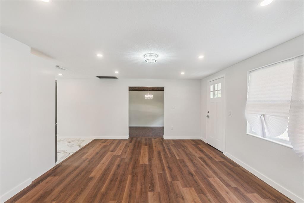 A bright, open-concept living room features wood-look flooring, white walls, and a white front door — 126 KENSINGTON ROAD, DELAND, FL