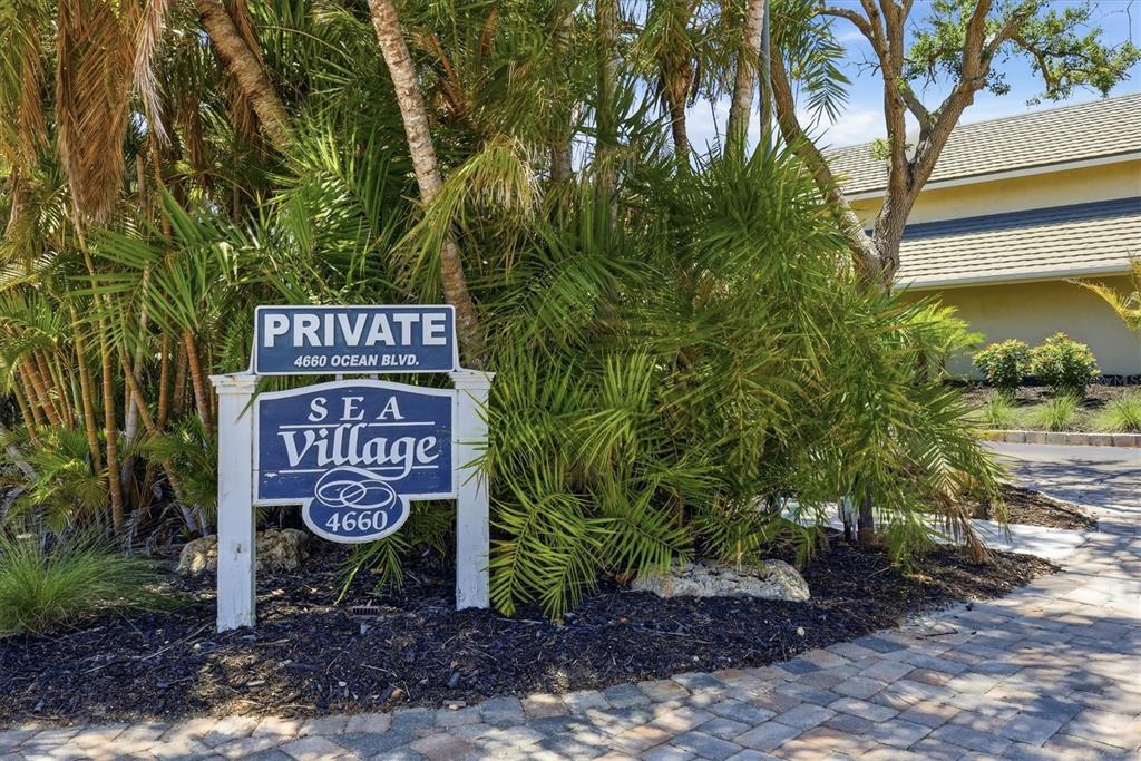 A sign for Sea Village stands in a landscaped area with palm trees and pavers — 4660 OCEAN BOULEVARD UNIT Q2, SARASOTA, FL