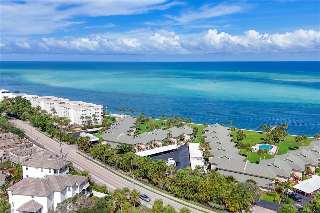 An aerial view shows a coastal residential complex with palm trees, parking, and turquoise water — 4660 OCEAN BOULEVARD UNIT Q2, SARASOTA, FL