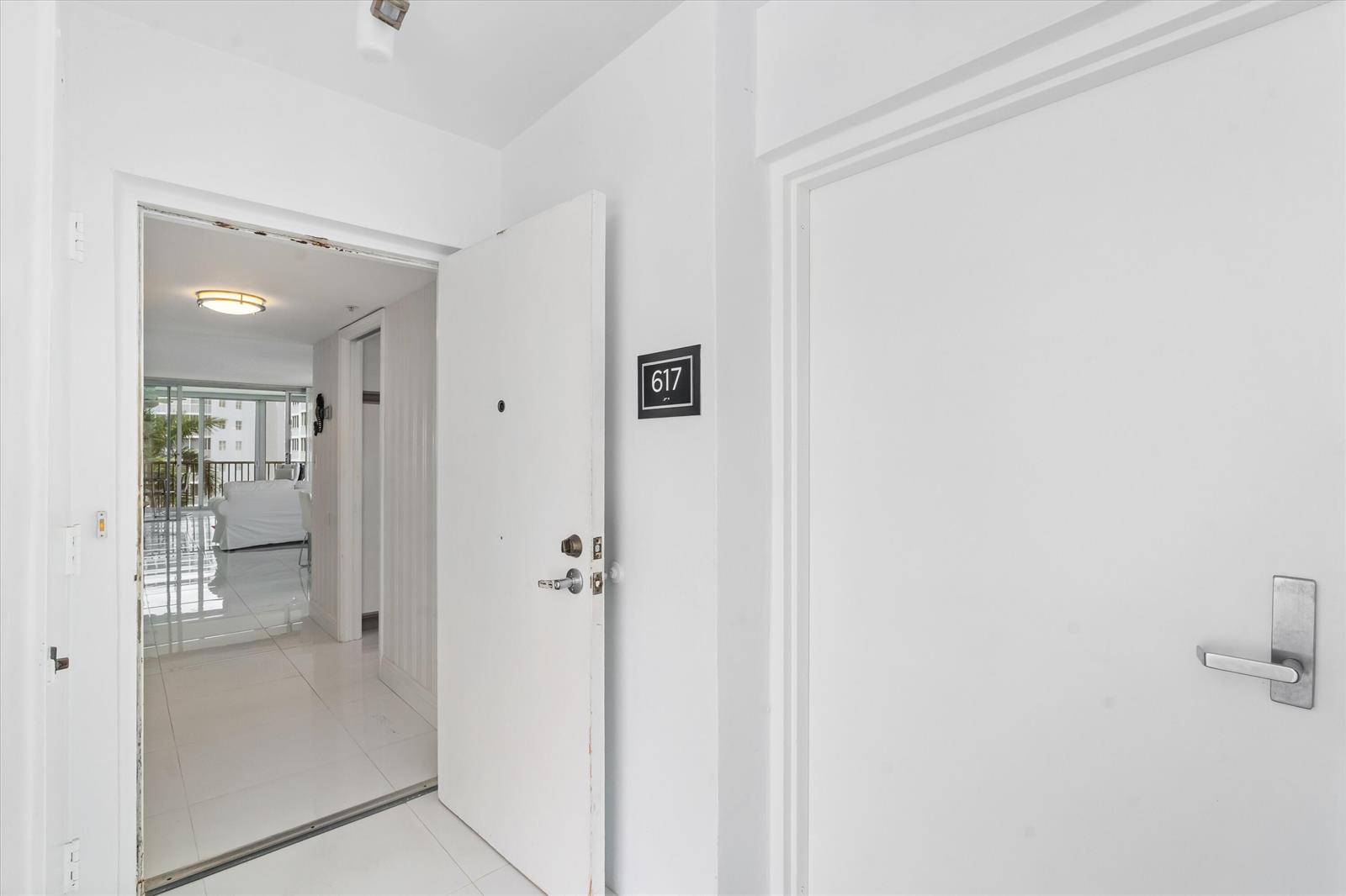 An open apartment door reveals a white-tiled hallway leading to a bright living space — 3300 S Ocean Boulevard # c, Highland Beach FL 33487, HIGHLAND BEACH, FL